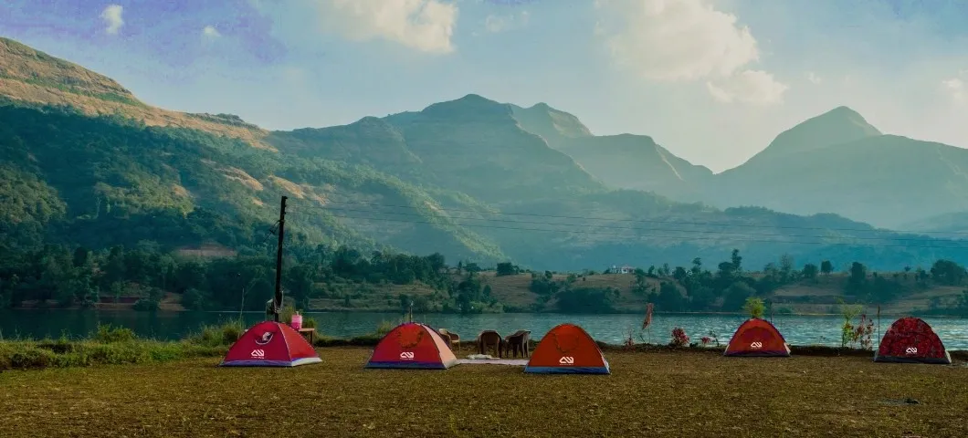 Red tent pitched on a rocky outcrop overlooking forested hills, banner image