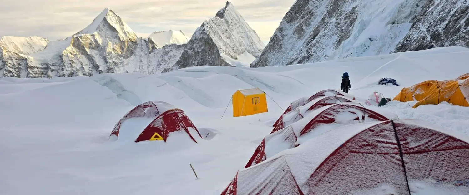Row of red tents at a campsite beside a misty mountain lake